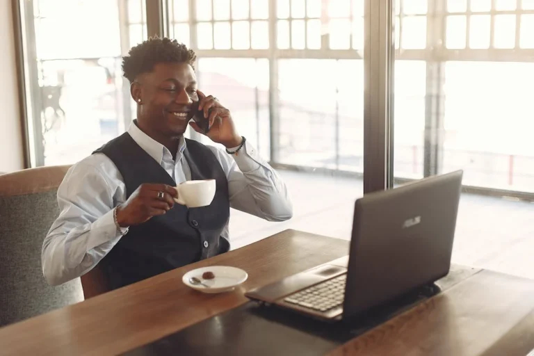 Illustrative photo: a person drinks coffee at a desk while talking on a phone in front of their laptop, and hopefully it's a good coffee paid for with an embedded finance spendable caffeine allowance