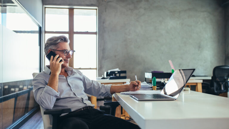 Illustration photo: a business person sitting at a desk on the phone in a modern minimal office environment
